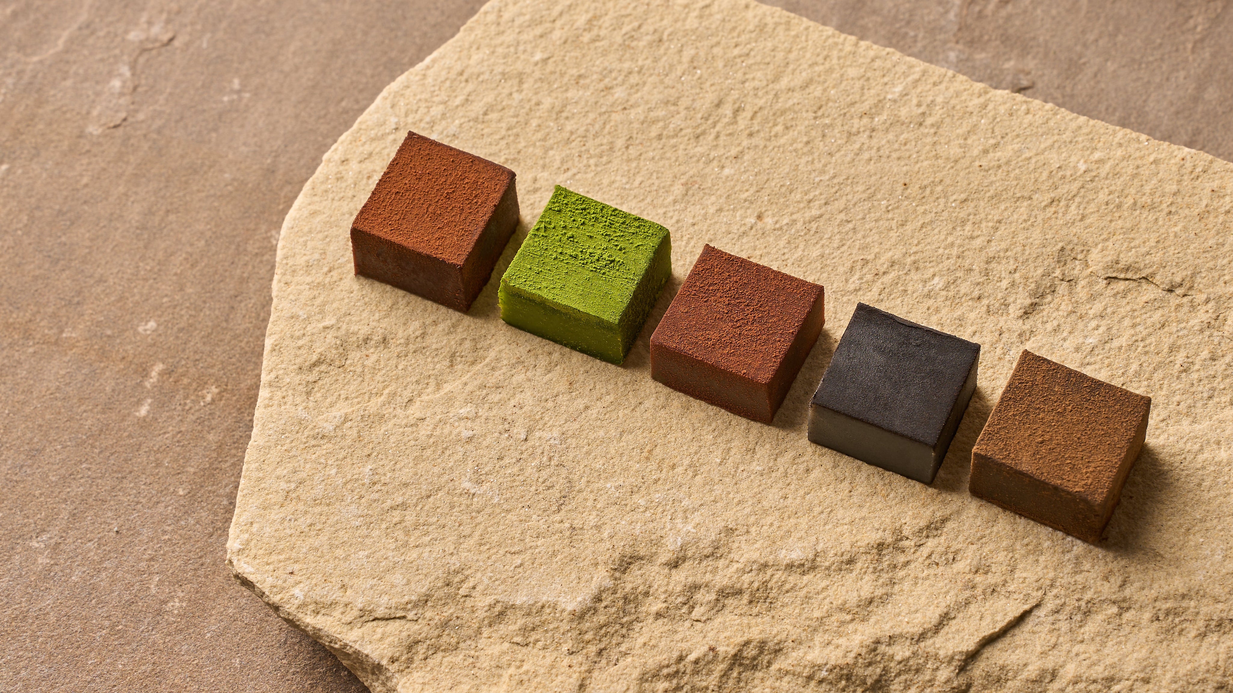 Five square blocks in different colors arranged on a textured stone surface